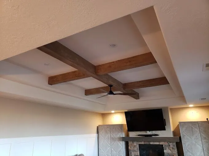 Ceiling with exposed wooden beams, a ceiling fan, and recessed lighting. Below, a wall-mounted TV, fireplace, and two cabinets are visible.