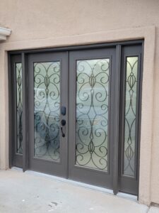 A dark metal-framed glass door with decorative wrought iron patterns, flanked by two matching sidelights, set in a stucco wall.