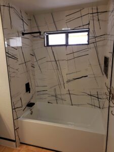A bathroom with a bathtub, abstract patterned wall tiles, a window above, and a black showerhead.