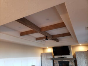 Ceiling with wood beams and a ceiling fan. A flat-screen TV is mounted above a stone fireplace, and two cabinets flank the fireplace.