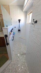 A modern shower with white subway tiles and a glass partition. It features black fixtures, a built-in shelf with toiletries, and a small window.
