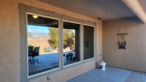 Patio with beige walls, a large window reflecting outdoor trees and furniture, a hanging decor piece, and a white bucket on the floor.