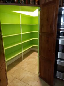 A corner pantry with bright lime green walls, white shelving, and wooden doors, adjacent to stainless steel kitchen appliances.