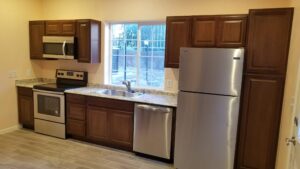 Modern kitchen with dark wood cabinets, stainless steel appliances including a fridge, oven, microwave, and dishwasher, and a window above the sink.
