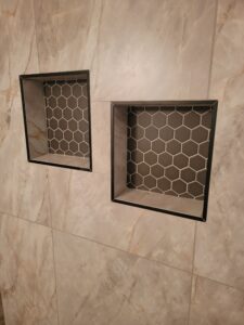 Two recessed shelves with hexagonal tile patterns set into a marble-tiled wall.